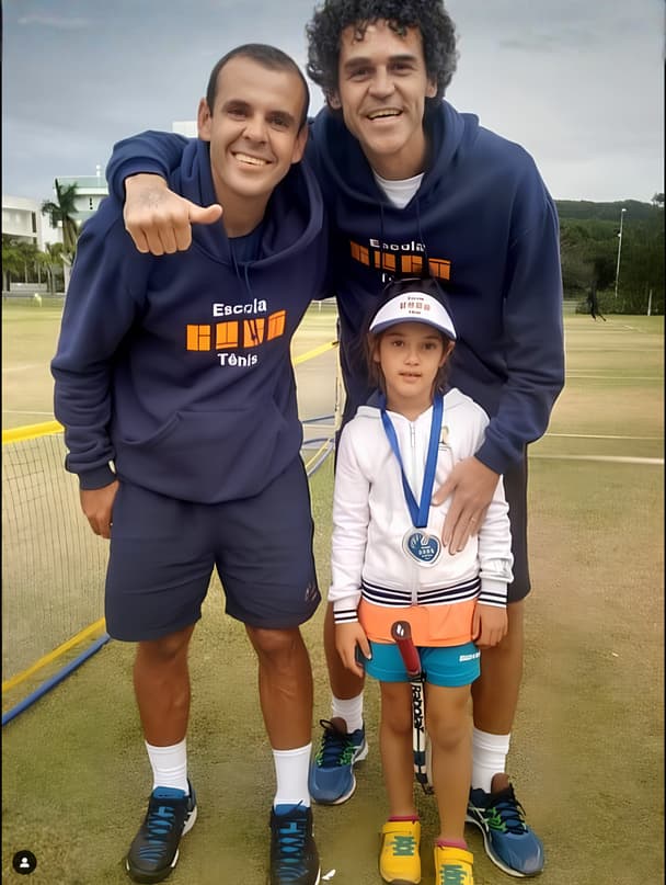 Duda criança com medalha, ao lado de dois tenistas