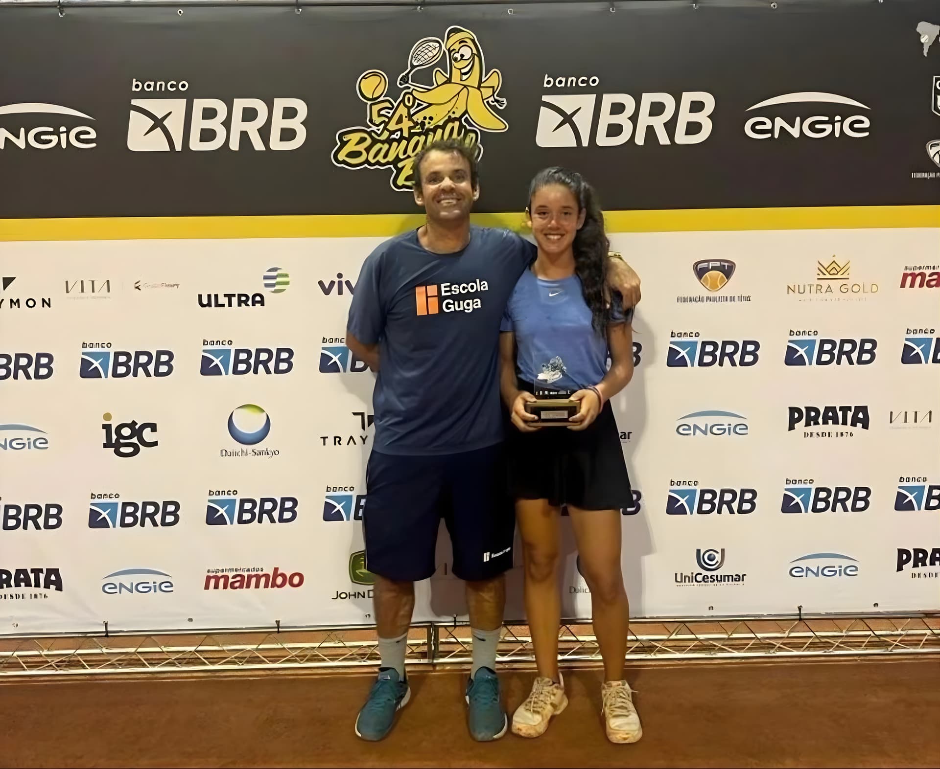 Duda no pódio com troféu ao lado do treinador