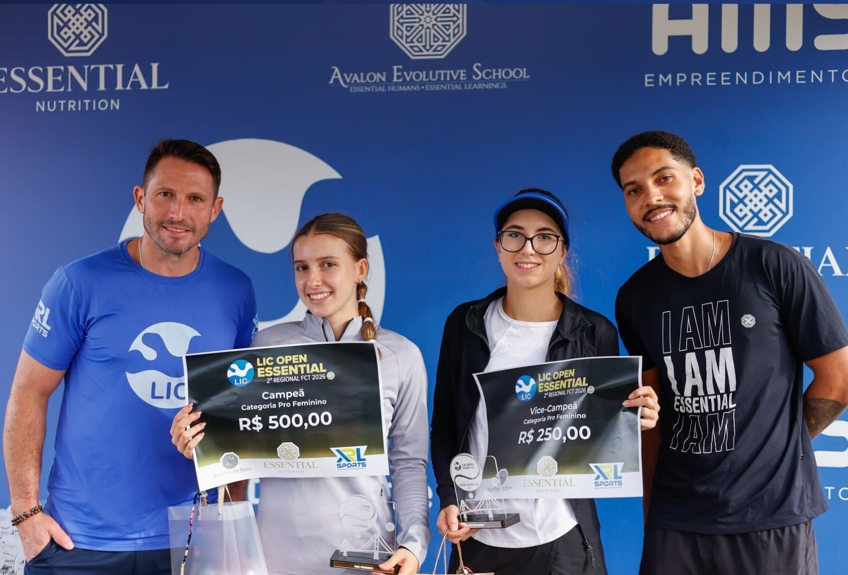 Campeãs recebendo premiação em frente ao backdrop de patrocinadores